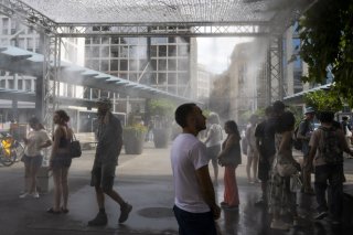 Image d'illustration: des personnes profitent d'un brumisateur géant installé par la ville de Geneve afin de se rafraichir durant la canicule, à Genève, en juillet dernier. KEYSTONE/MARTIAL TREZZINI