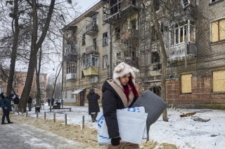 Une femme porte une couverture distribuée par l'agence des Nations Unies pour les réfugiés (HCR) près du site d'une frappe russe sur un immeuble à Kharkiv. KEYSTONE/EPA/SERGEY KOZLOV