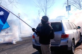 Un drapeau de l'Etat du Minnesota brandi alors que les agents fédéraux de l'immigration lancent des gaz lacrymogènes, samedi à Minneapolis. KEYSTONE/AP/Abbie Parr