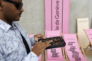 Ali a en main parcourt du bout de ses doigts la fiche du boîtier Virtuoz, un dispositif qui lui permet de se déplacer de façon autonome dans le bâtiment de la Comédie.