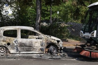Un employé municipal nettoie la rue près d'une voiture incendiée mercredià Nanterre.